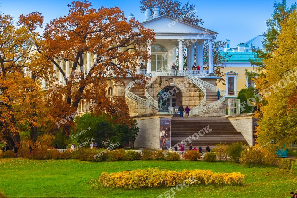 На фотографии изображена Камеронова галерея в Екатерининском парке Царского Села. Галерея, построенная по проекту архитектора Чарльза Камерона, известна своей элегантной архитектурой и монументальной лестницей. Осенние деревья вокруг галереи подчеркивают величие сооружения и добавляют теплые цвета в композицию. Этот архитектурный памятник является популярным местом для прогулок и изучения культурного наследия России.